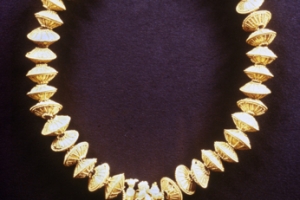  Περιδέραιο από το Άρσος. Αποτελείται από χρυσές ψήφους καλυμμένες με κοκκιδωτό διάκοσμο και κυλινδρικό περίαπτο από αχάτη με χρυσά επικαλύμματα, δύο ουραίους με στέμματα της Άνω και Κάτω Αιγύπτου και μια μέλισσα ανάμεσά τους. Κυπρο-Αρχαϊκής Ι περιόδου (750 – 600 π. Χ.)